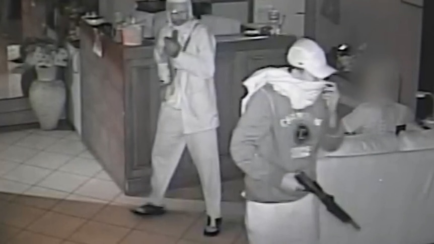Two men in a building, one of whom is carrying a gun.