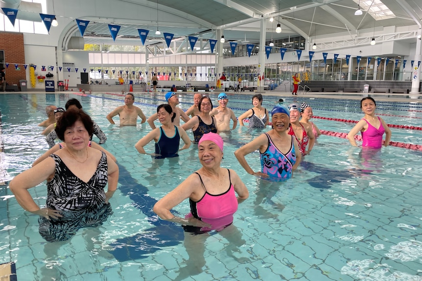 A group of older people smiling in the pool with their hands on their hips