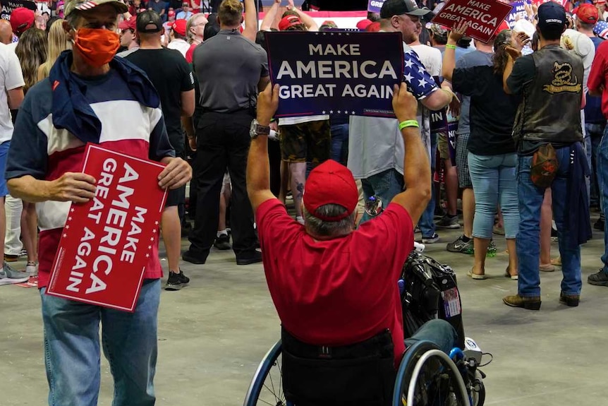 Man in wheelchair holds 'make America great again' sign with crowd in front of him