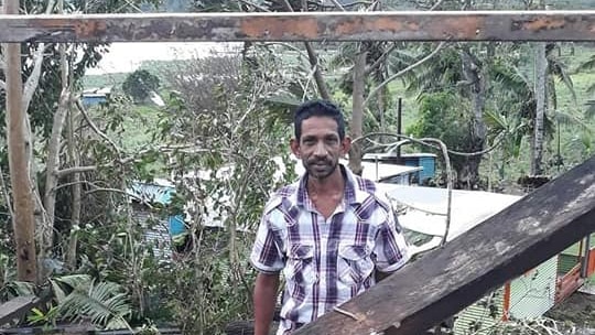 Anil Deo stands looking at the camera amid the ruins of a home.