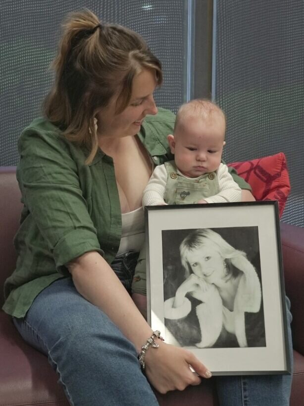 Iris Leeson sits with her baby on her lap, holding a photo og her