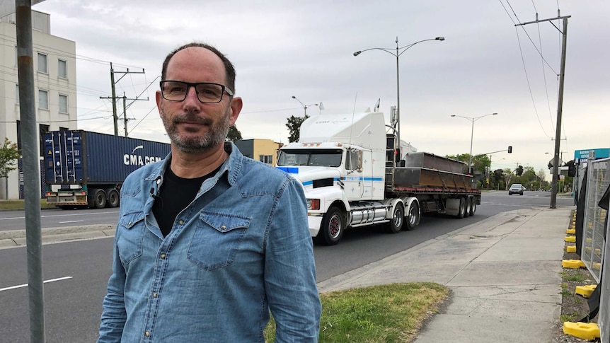Martin Wurt stands next to a road with trucks driving on it.
