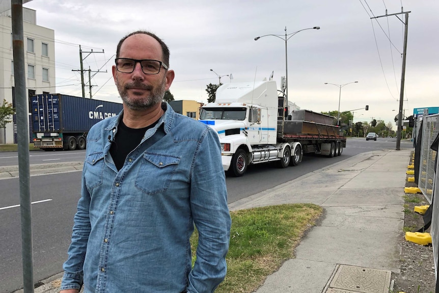 Martin Wurt stands next to a road with trucks driving on it.