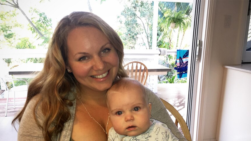 Illawarra mother Natalie Zukowski smiles at camera. Her baby son Liam is sitting on her lap.