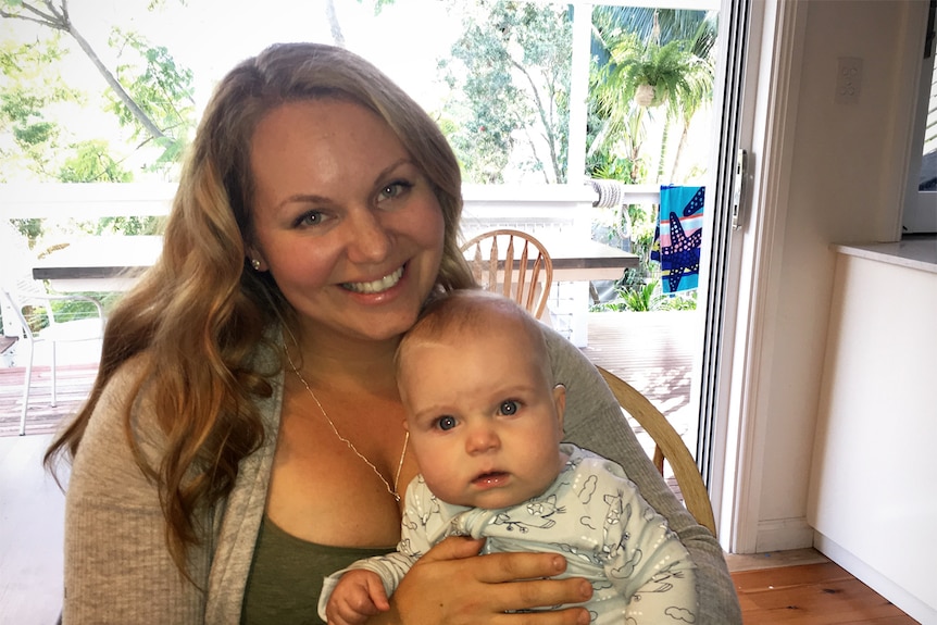 Illawarra mother Natalie Zukowski smiles at camera. Her baby son Liam is sitting on her lap.