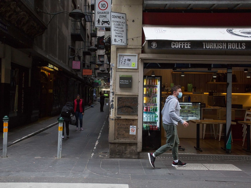 Two women take photos in the empty laneway, as a man wearing a mask walks past a cafe