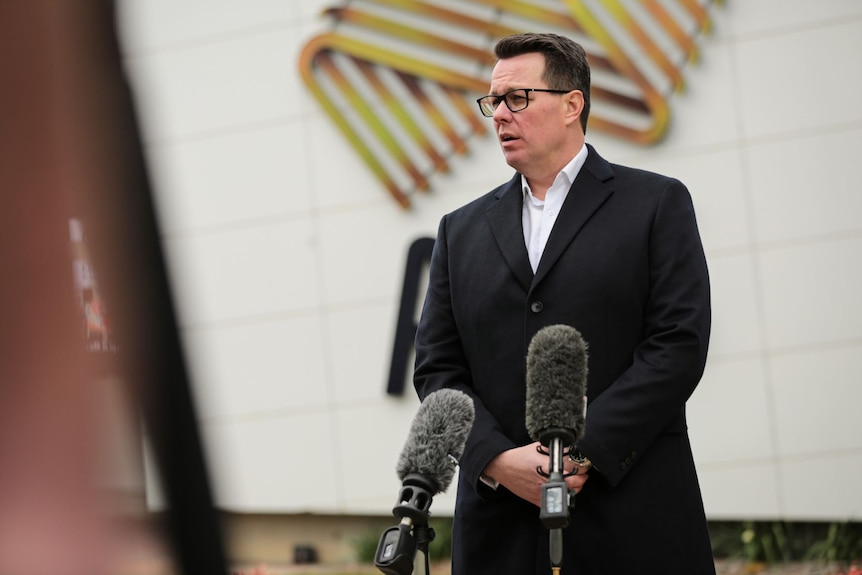 A man in a black suit stands at a lectern.