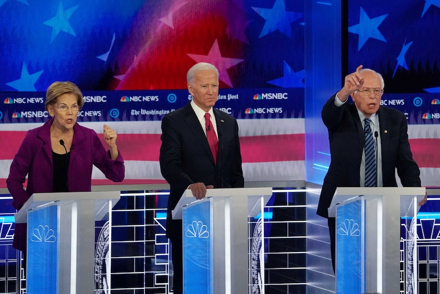 Elizabeth Warren, Joe Biden and Bernie Sanders stand on the primary debate stage