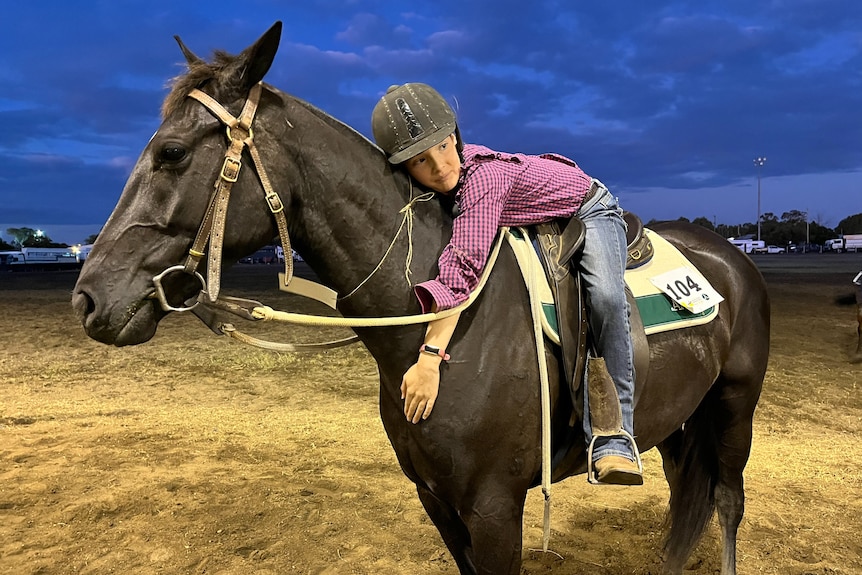 A young girls lays across a horse at dusk in an outback setting