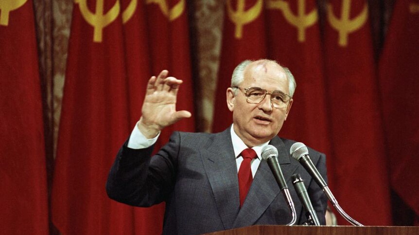 Mikhail Gorbachev stands in front of microphones while addressing business executives