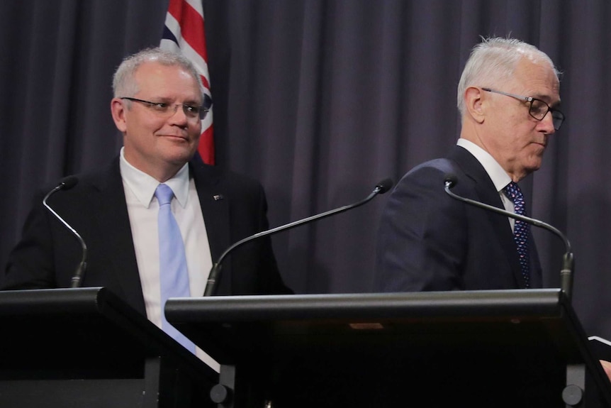 Scott Morrison smiles in the direction of Malcolm Turnbull's back, as they both move to walk away from a podium.