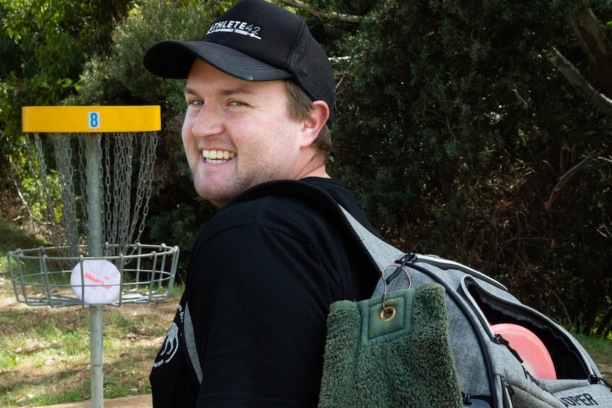 Disc golf player looks over shoulder to smile, a disc sitting in the basket behind.
