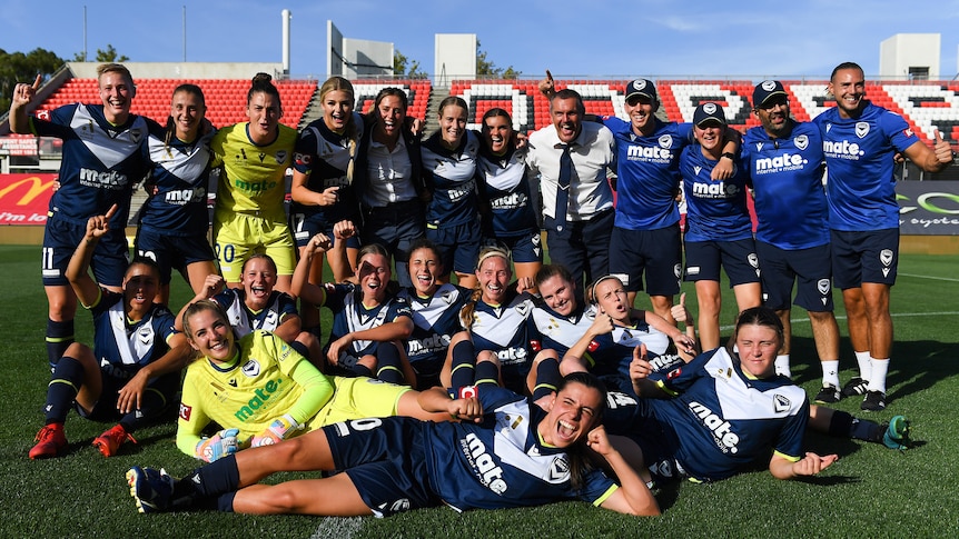 Soccer players wearing navy blue pose for a photo after winning a game