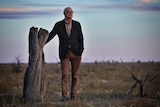 Ross Garnaut leans on a dead tree.