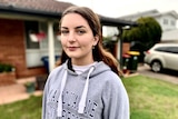 Woman in Macquarie University hoodie looks at the camera outside a house.