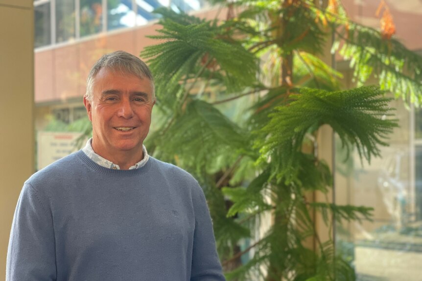 White man with grey hair standing in front of a tree in a foyer