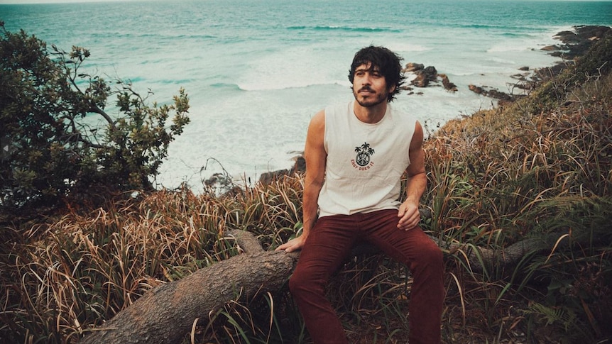 morgan evans sits on a fence in front of the ocean, he's looking out into the distance