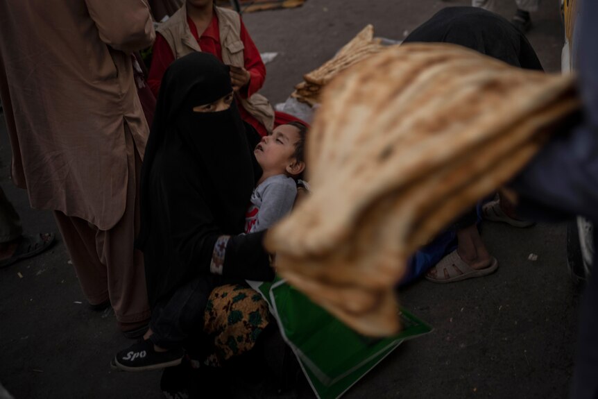 A woman in a black burka holds a sleeping child. 