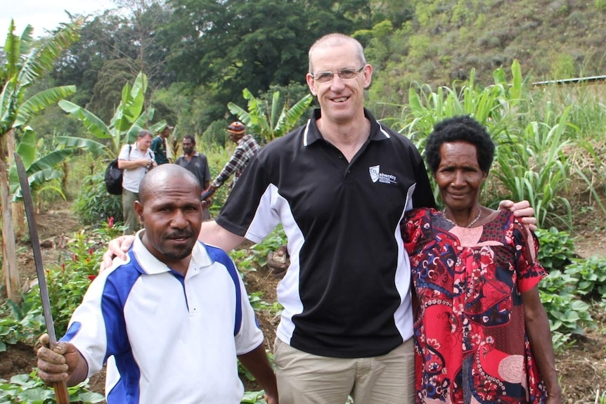 A man stands between to farmers from Papua New Guinea