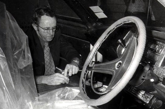 A black and white picture of a WA Police detective looking inside a car for evidence with plastic covering the front seat.