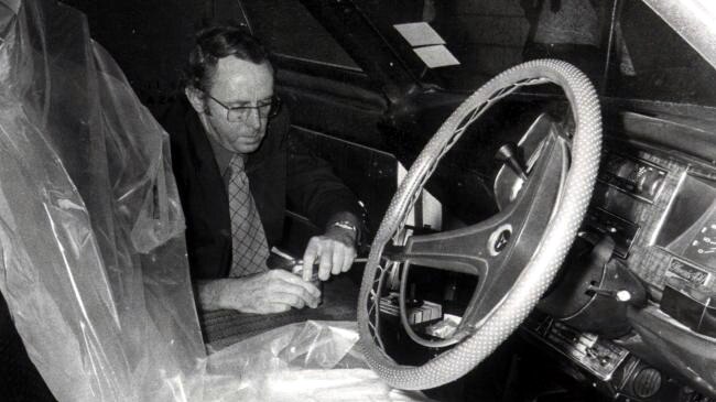 A black and white picture of a WA Police detective looking inside a car for evidence with plastic covering the front seat.
