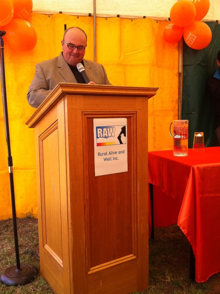 A man speaks at a lectern bathed in orange light.