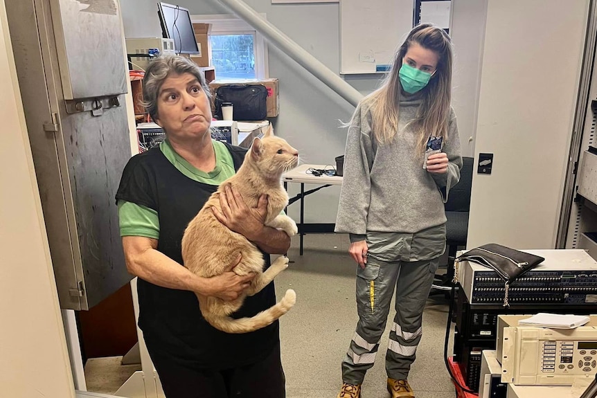 Woman holding a cat while another woman looks on.