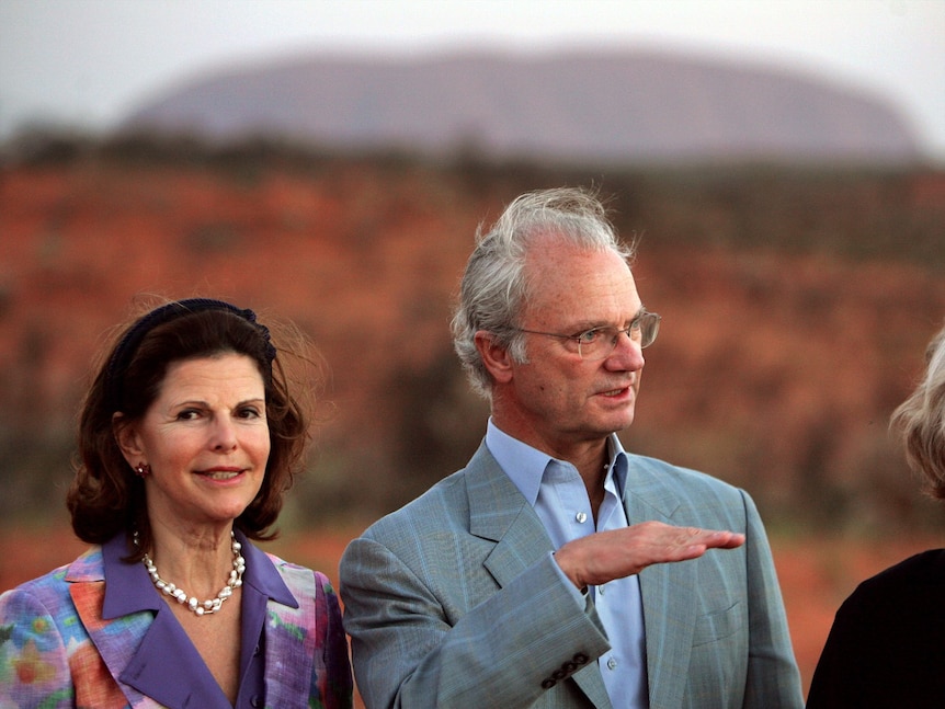 A woman looks at the camera while a man gestures with a hand and looks on