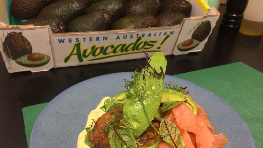 Plate of rich green avocadoes and smoked salmon in front of tray of avocadoes