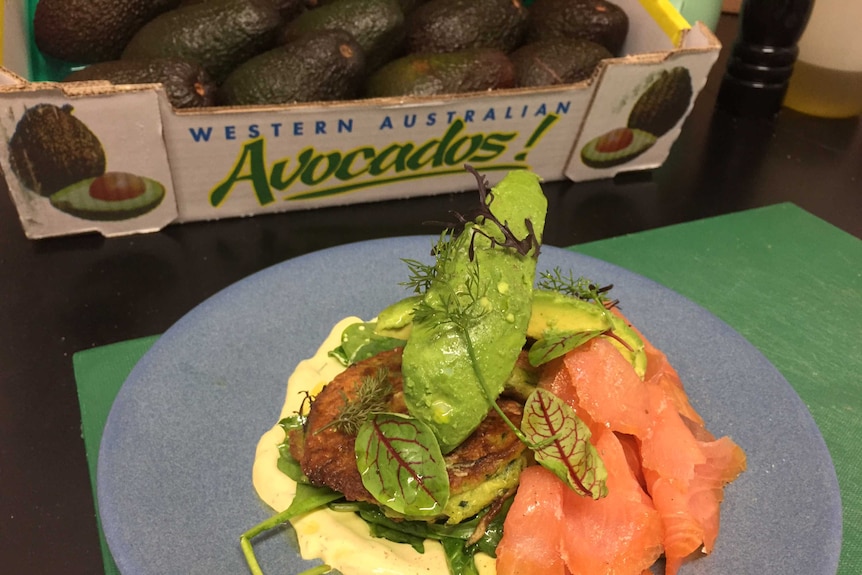 Plate of rich green avocadoes and smoked salmon in front of tray of avocadoes