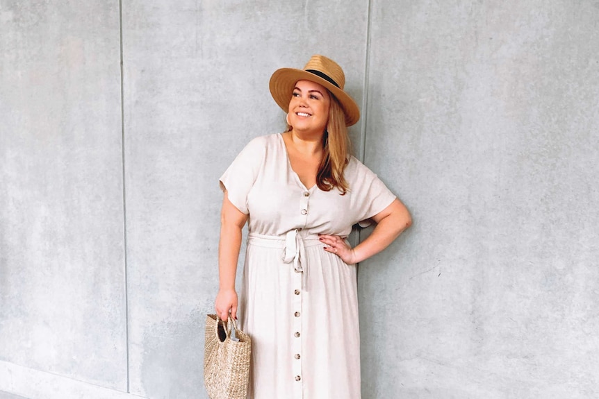 A young woman is wearing a large sunhat and a long, pale coloured-dress with buttons