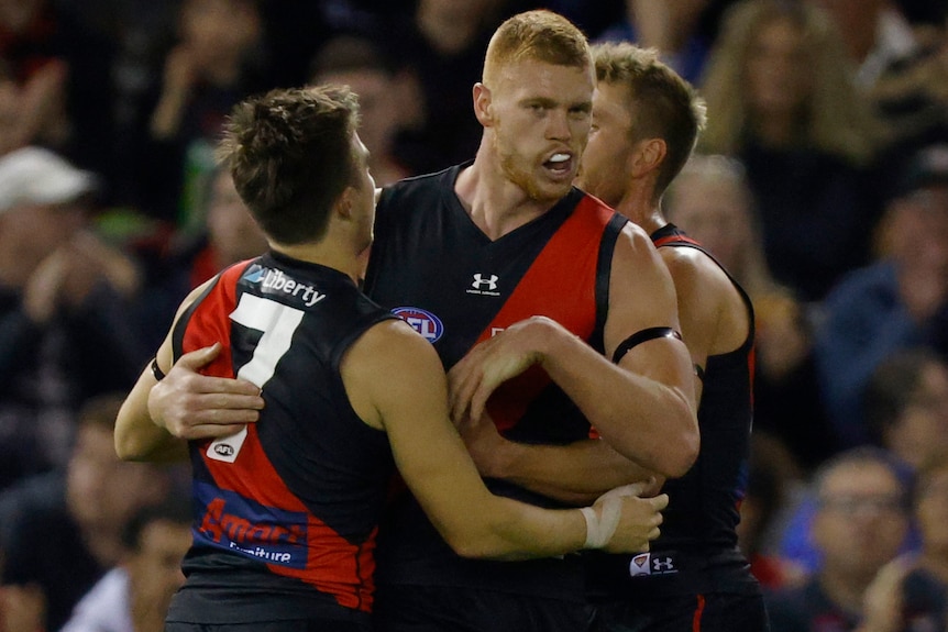 Three Essendon AFL players celebrate a goal against North Melbourne.