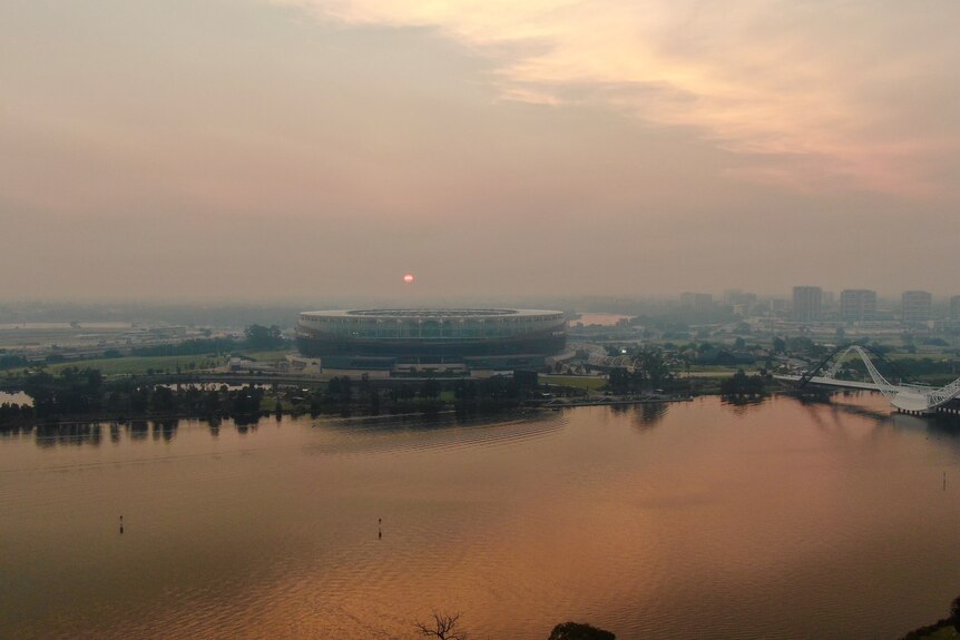 Smoke haze engulfs Perth Stadium as the sun rises over the Swan River
