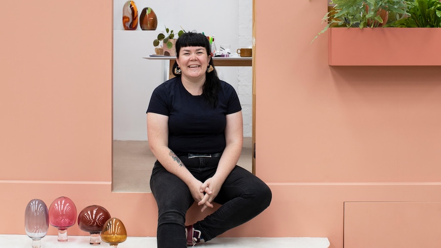 woman in black tee-shirt and jeans sitting on step with various glass objects