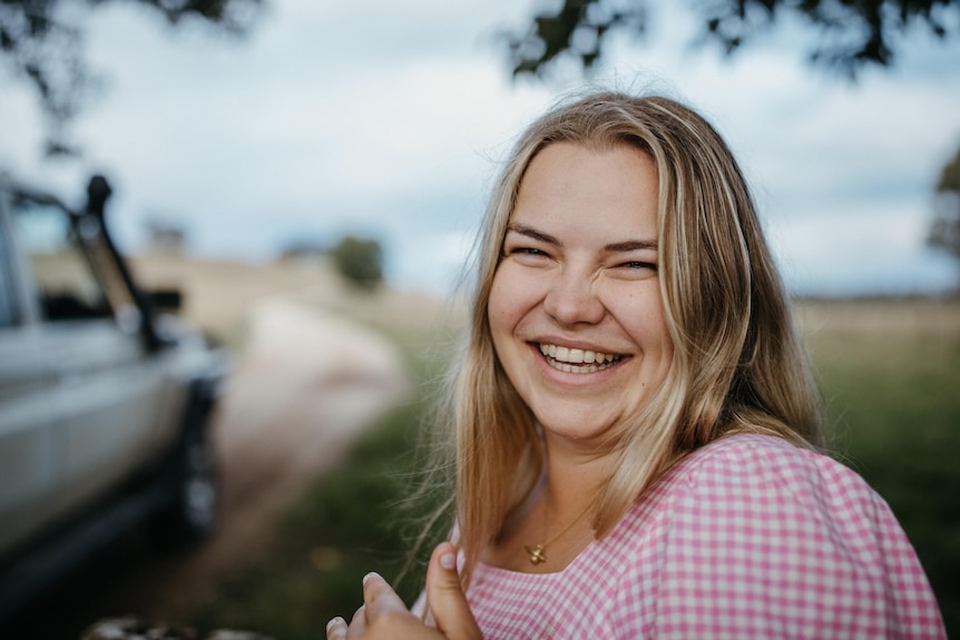 A young woman with blonde hair and a pink shirt smiles for the camera.