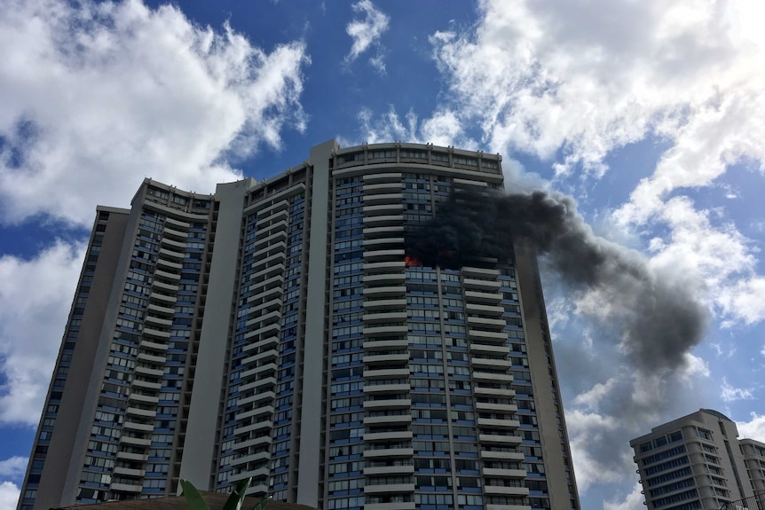 Billowing smoke and flames visible in a flat near the top of the high-rise apartment building.