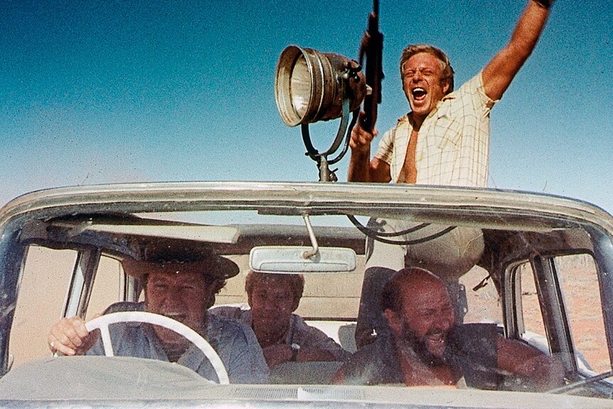 The cast members face the camera, all piled into a car with Jack Thompson popping out of the sun roof.