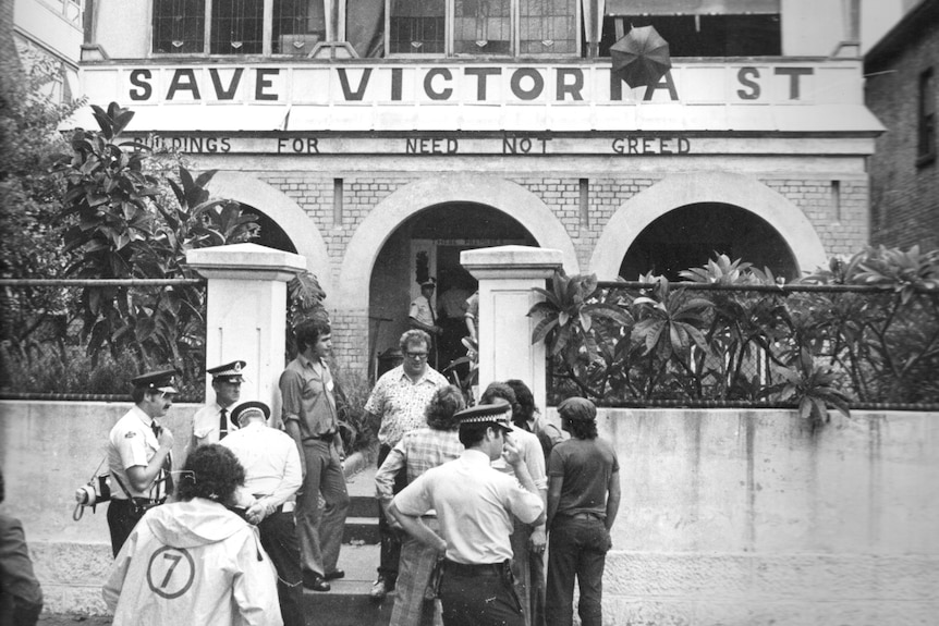 A crowd of people outside a terrace houses painted with the words 'Save Victoria Street'.