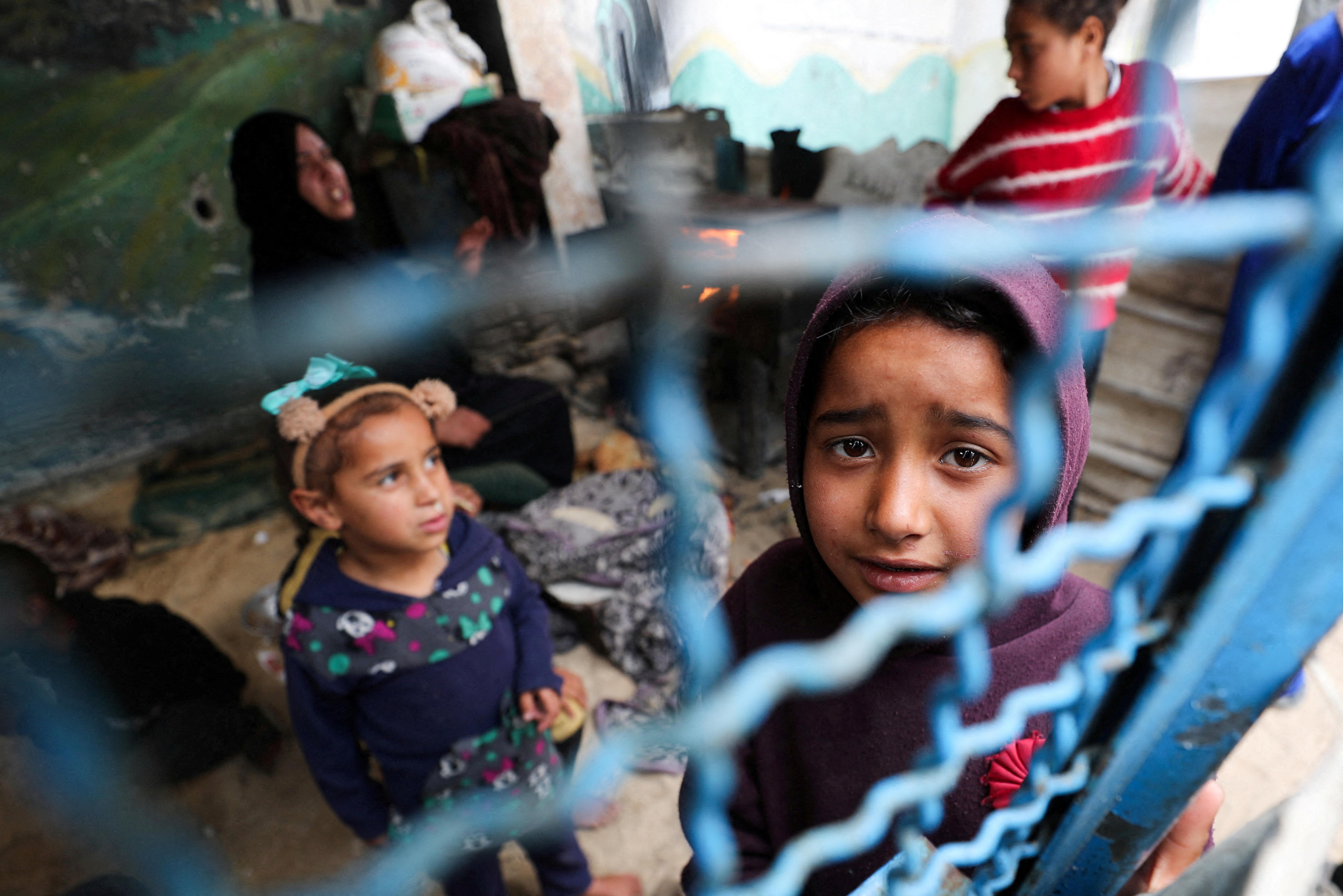 A young child looks sadly up through a fence 