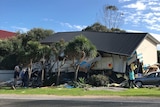 A two-storey white house with a grey roof destroyed by the impact of a truck crash.