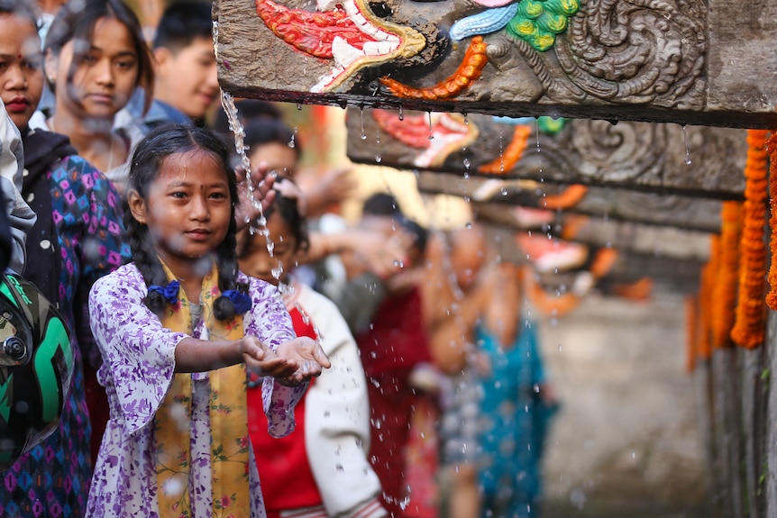 A young girl has her turn to wash her hands under colouful ceremonial taps as part of a Hindu ritual. 