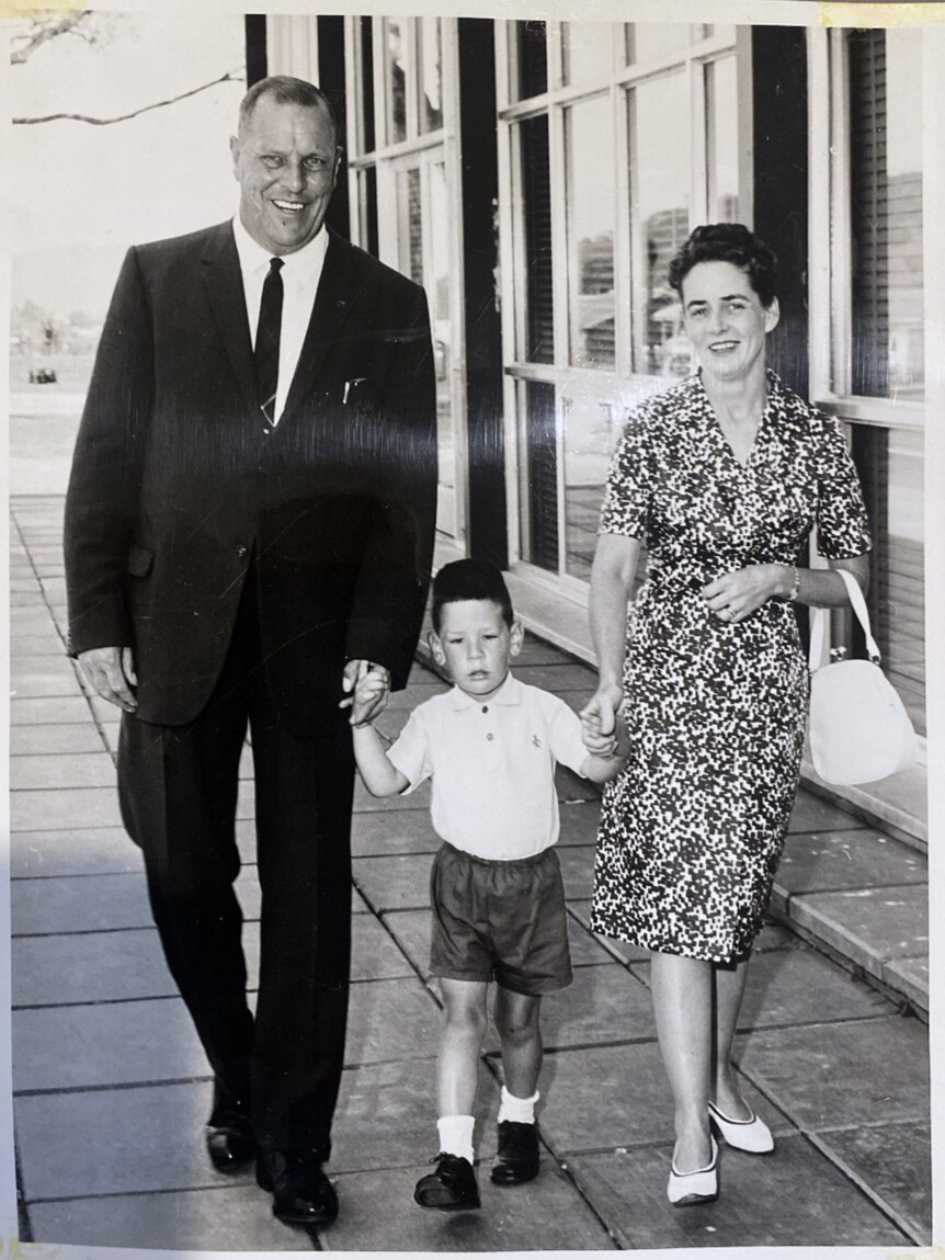 A black and white photo of a young boy holding the hands of his father and mother.