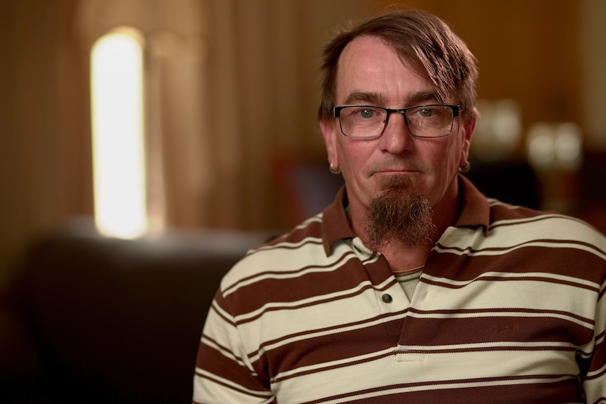 A man with a goatee beard, brown hair and glasses wearing a polo shirt.