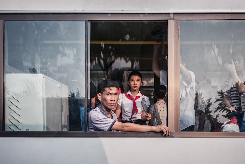 A North Korean man looks at the camera through the window of a bus.