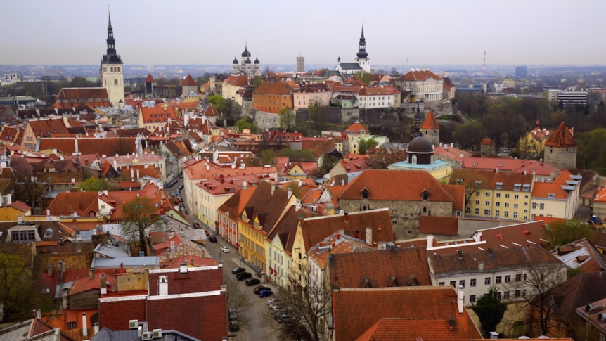 An aerial view shows a street winding between colourful buildings with church spires in the background.