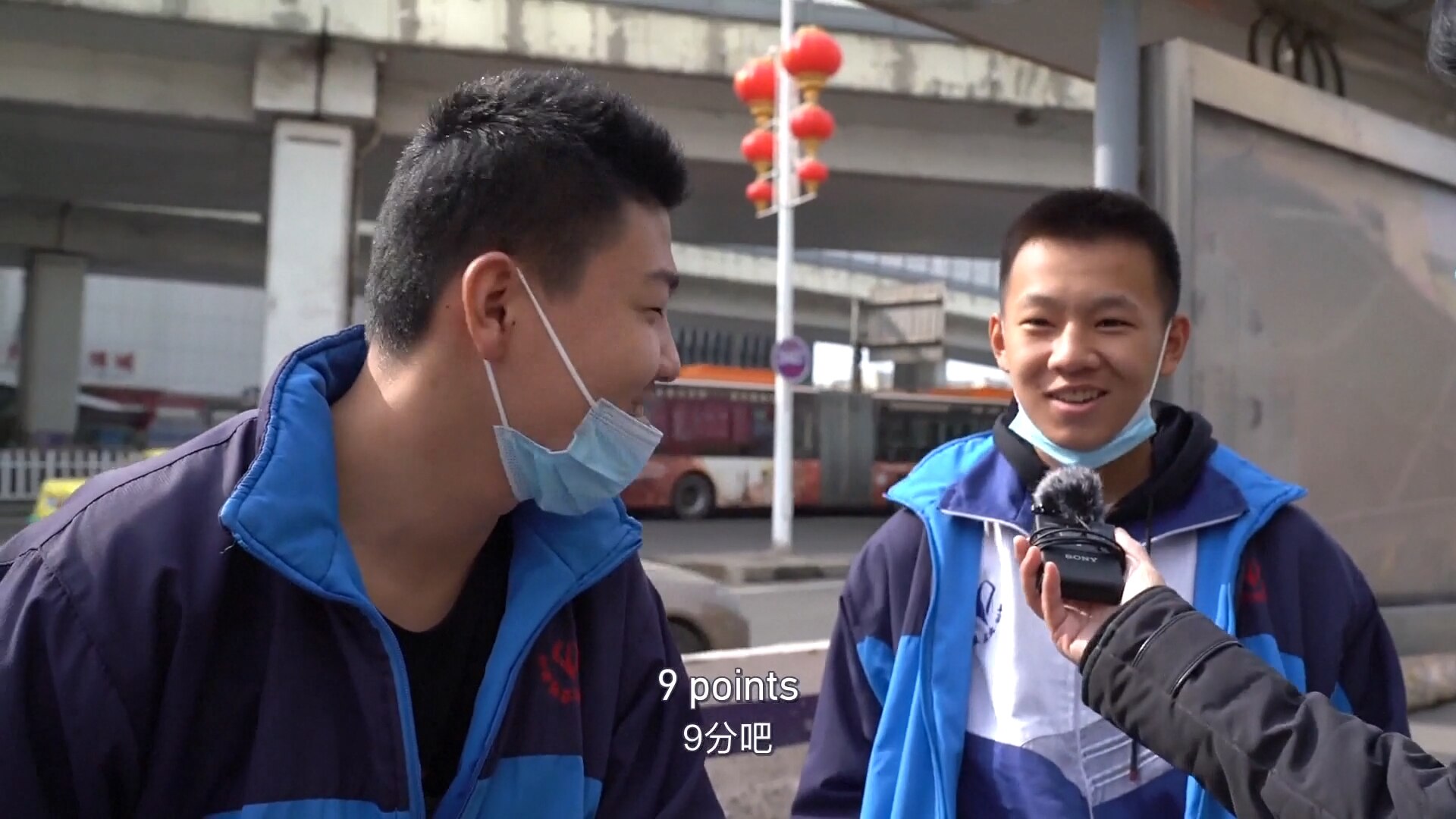 Two young men smile as they answer a question into a recording device being held by a third man who is not seen.