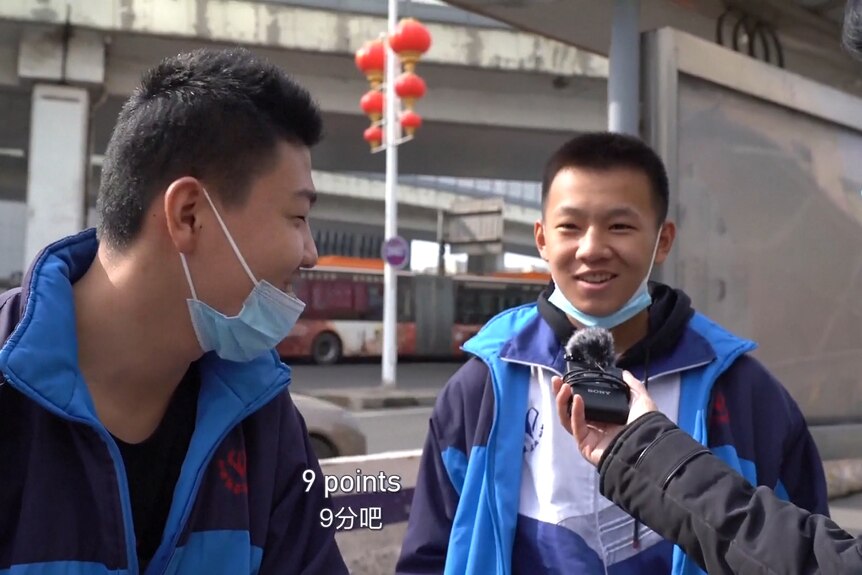 Two young men smile as they answer a question into a recording device being held by a third man who is not seen.