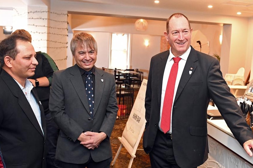 Fraser Anning wearing a suit and tie standing alongside three men at a cafe.