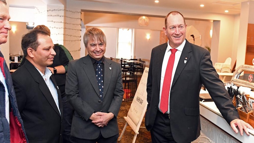 Fraser Anning wearing a suit and tie standing alongside two men at a cafe