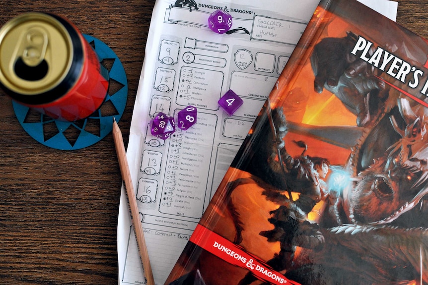 A Dungeons & Dragons Player's Handbook, a filled out character sheet, some purple dice, a pencil and a can of beer on a table.